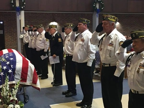 A group of men in military uniforms salute in front of an american flag