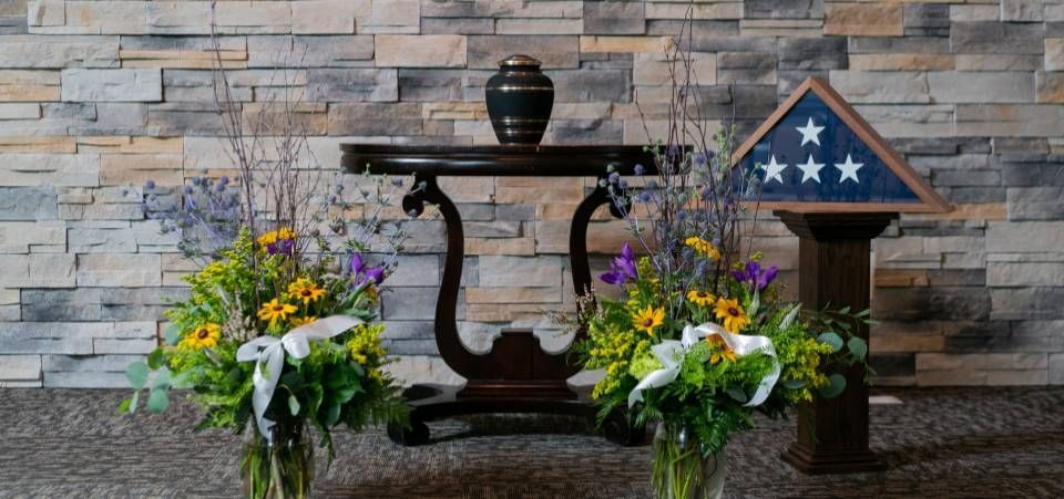 A table with flowers and a flag on it in front of a brick wall.