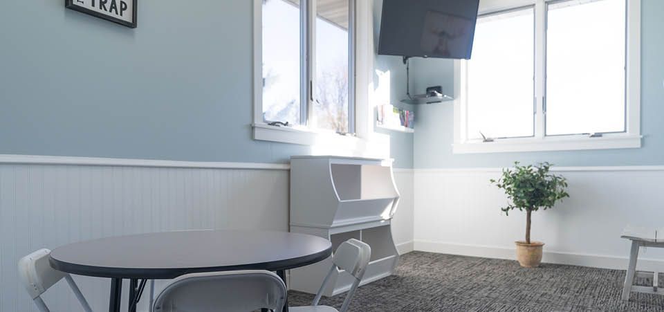 A living room with a table and chairs and a tv on the wall.
