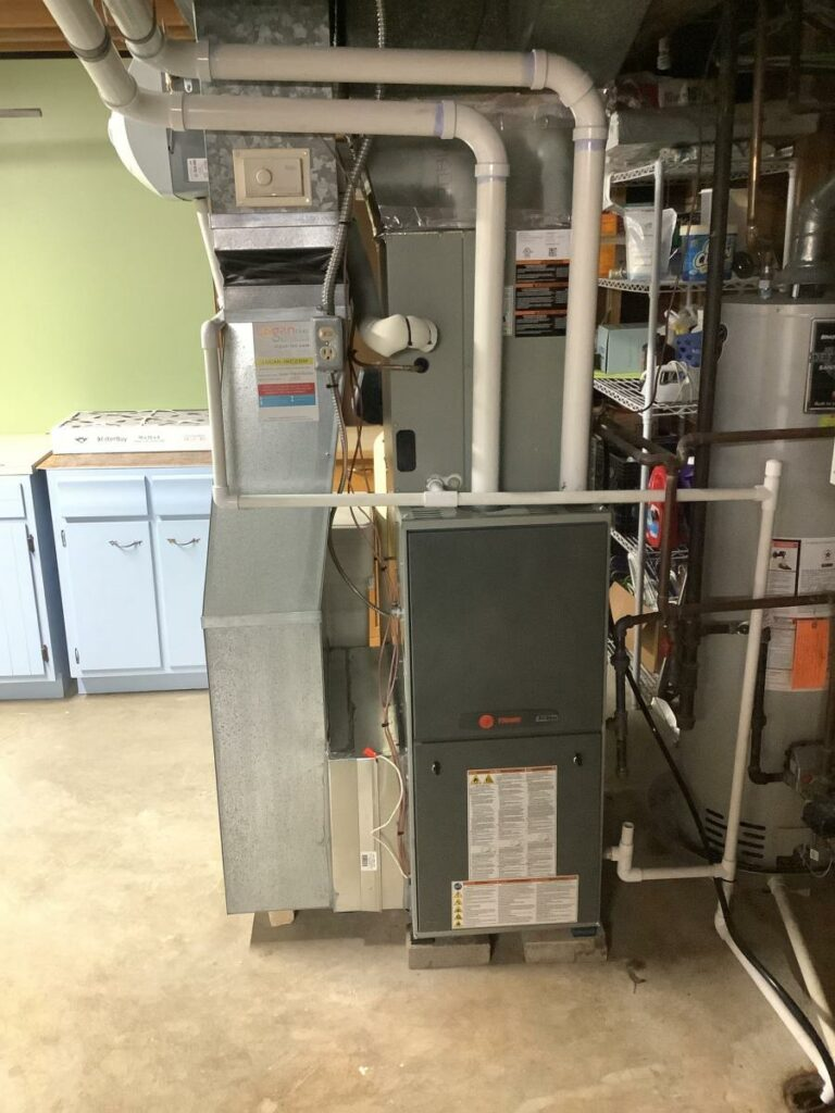 Furnace and hot water heater in a basement utility room. Gray and white appliances, neutral walls.