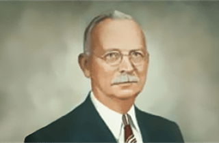 A man with glasses and a mustache is wearing a suit and tie