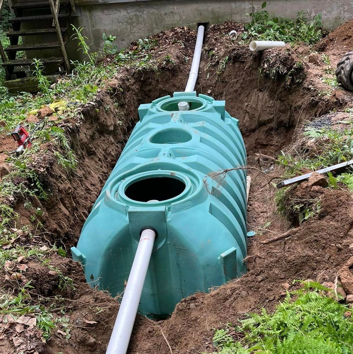 A green septic tank is being installed in a hole in the ground by Tailored Excavation