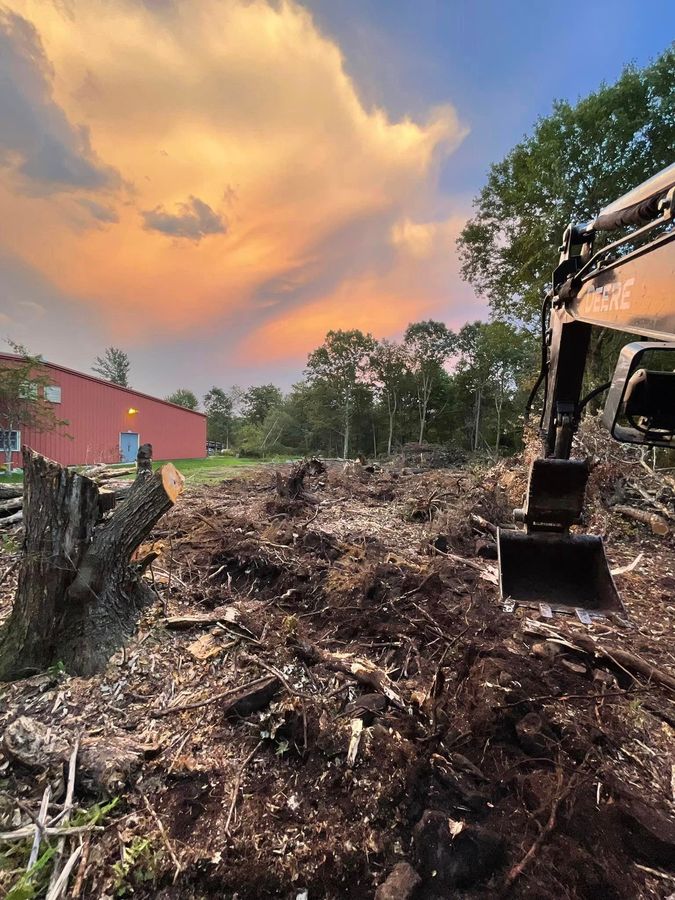 A large pile of dirt with a red building in the background by Tailored Excavation.