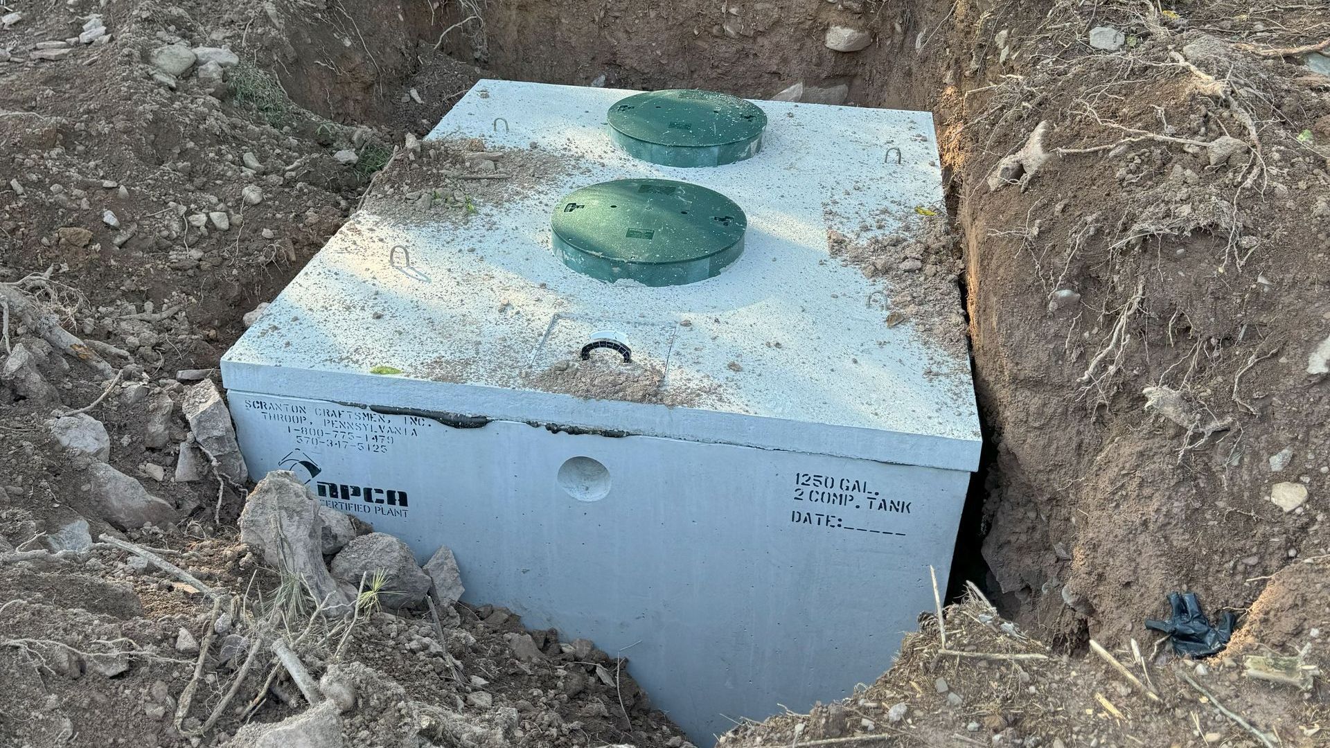 A green septic tank is being installed in the woods by Tailored Excavation.