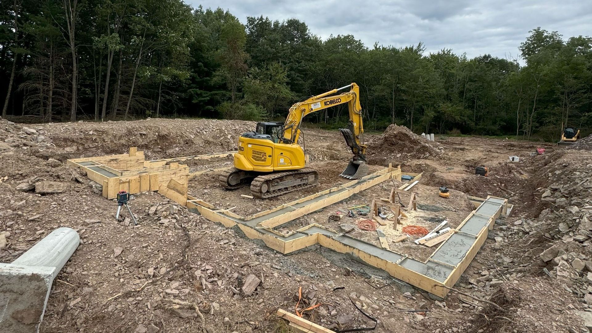 A large excavator bucket is sitting on top of a pile of rocks  by Tailored Excavation.
