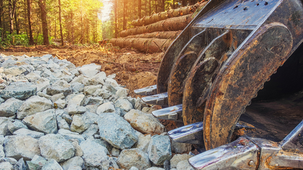 A large excavator bucket is sitting on top of a pile of rocks  by Tailored Excavation.