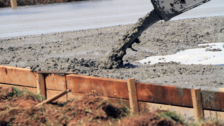 A person is pouring concrete into a hole in the ground by Tailored Excavation.