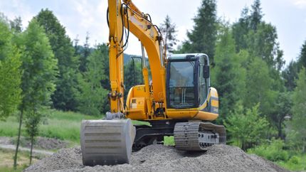 A yellow excavator is sitting on top of a pile of grave  by Tailored Excavation.