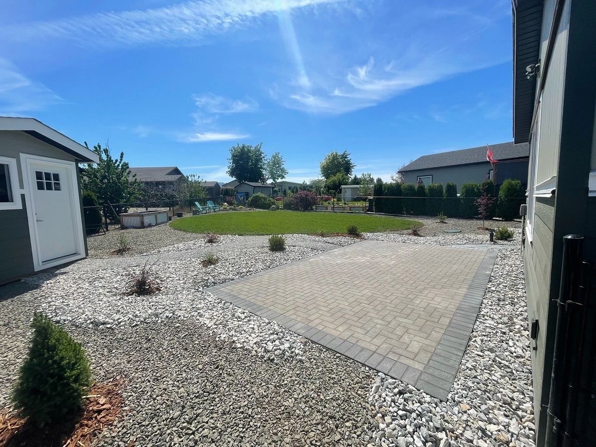 Backyard with gravel, paved patio, shed, lawn, and blue sky.
