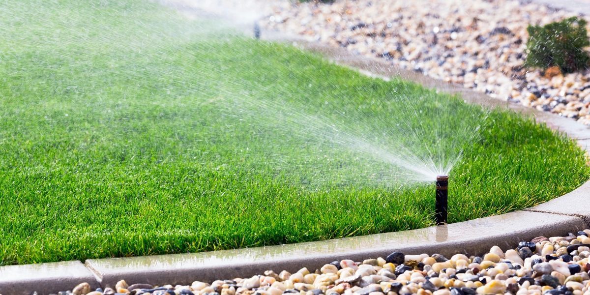 Lawn sprinkler watering green grass in a yard surrounded by small stones.