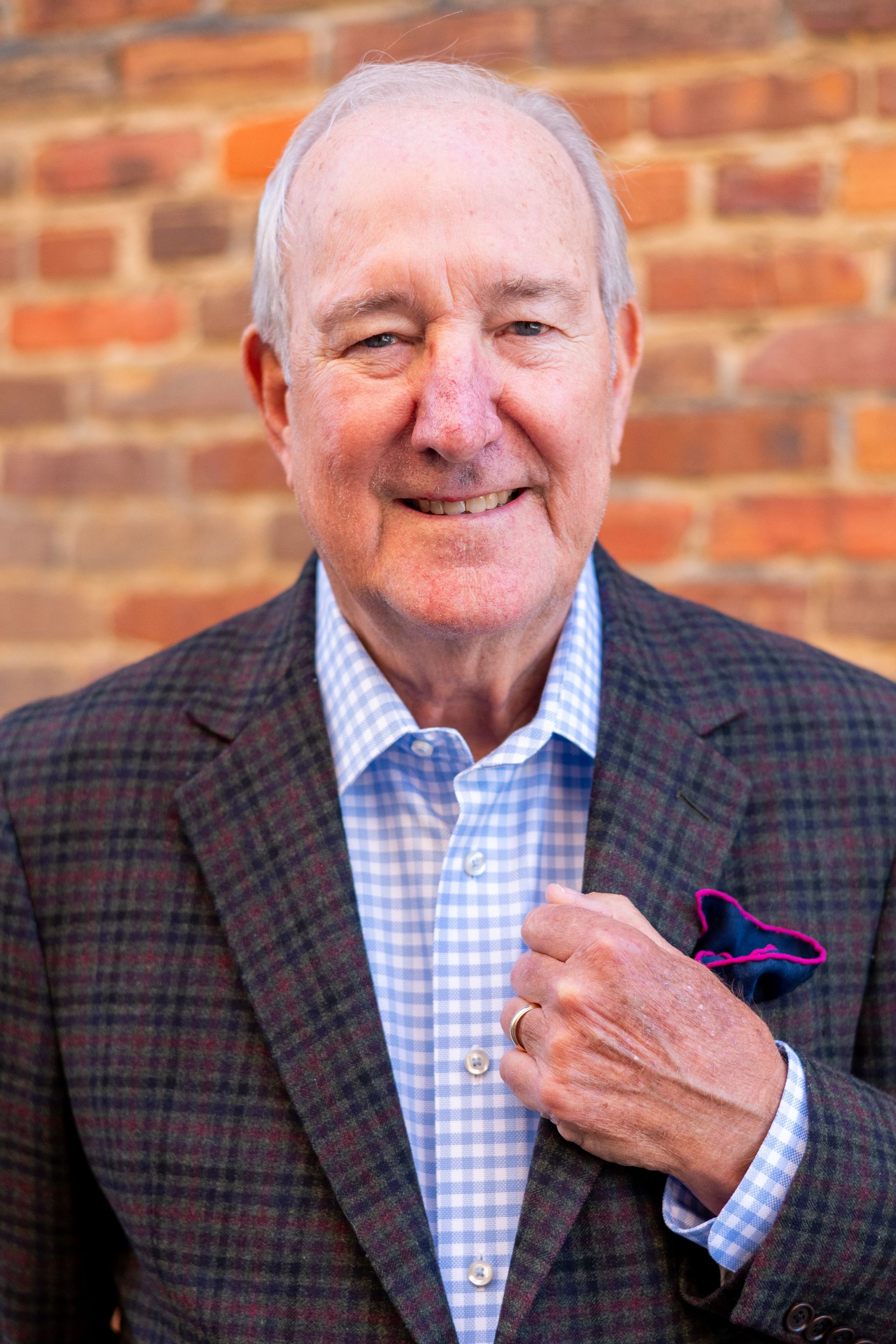 Man in plaid jacket, blue shirt, touching his jacket. Brick wall background.