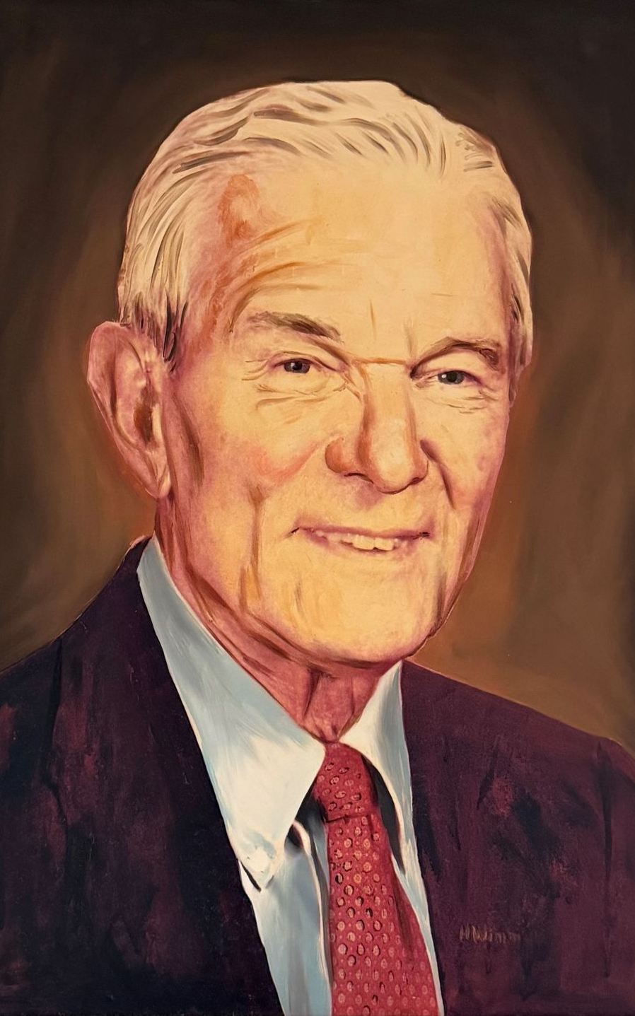 Portrait of an older man with white hair, smiling, wearing a suit and red tie.