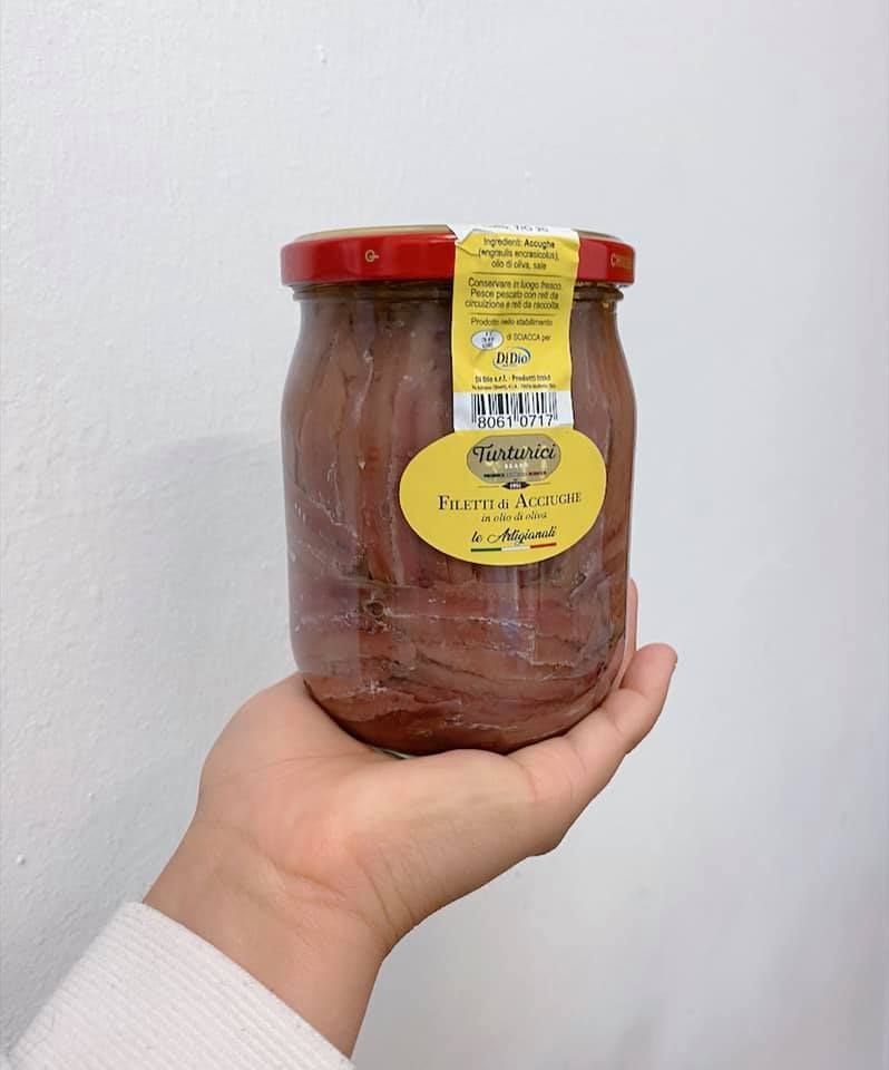 Mano che tiene un barattolo di acciughe con coperchio rosso ed etichetta gialla.