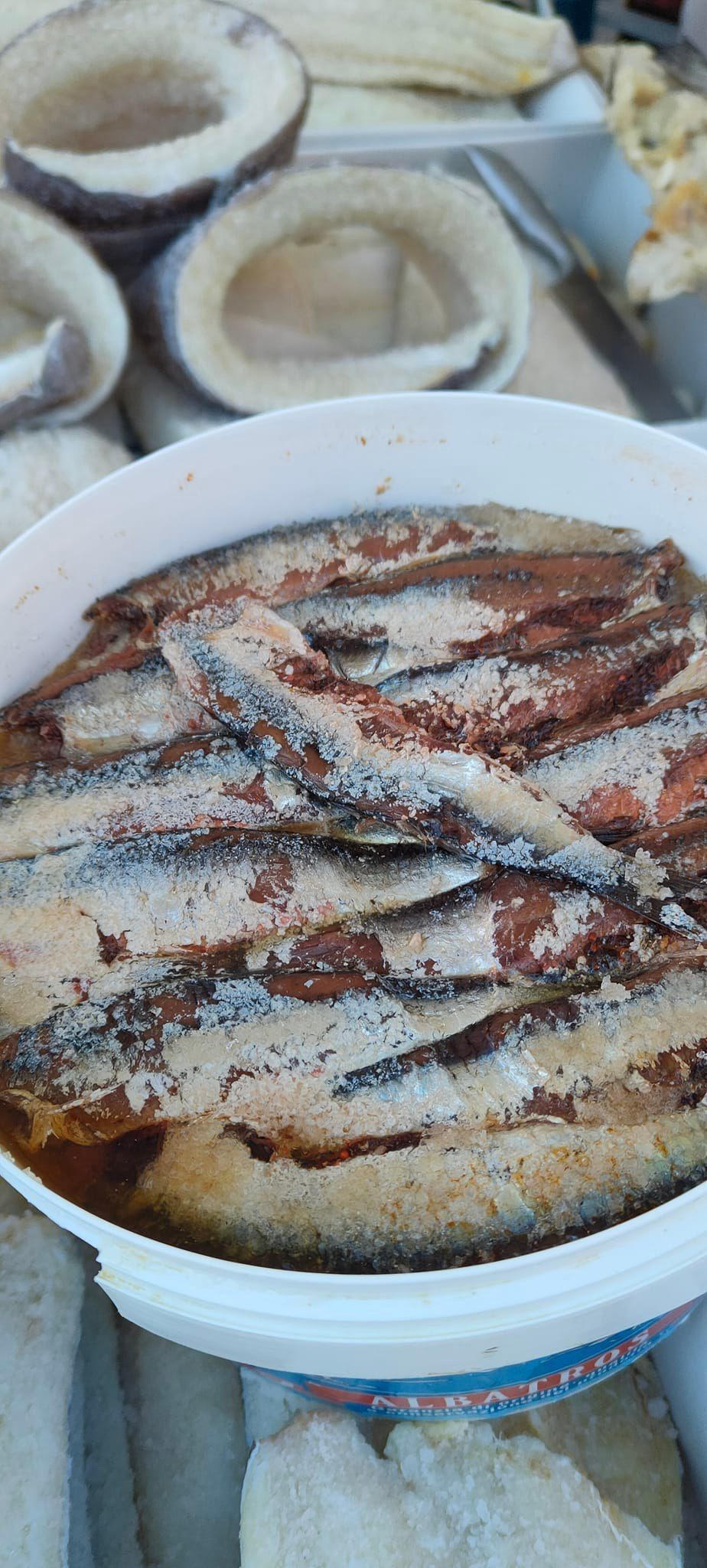 Secchio di acciughe salate, primo piano. Altri pesci e prodotti alimentari sullo sfondo.