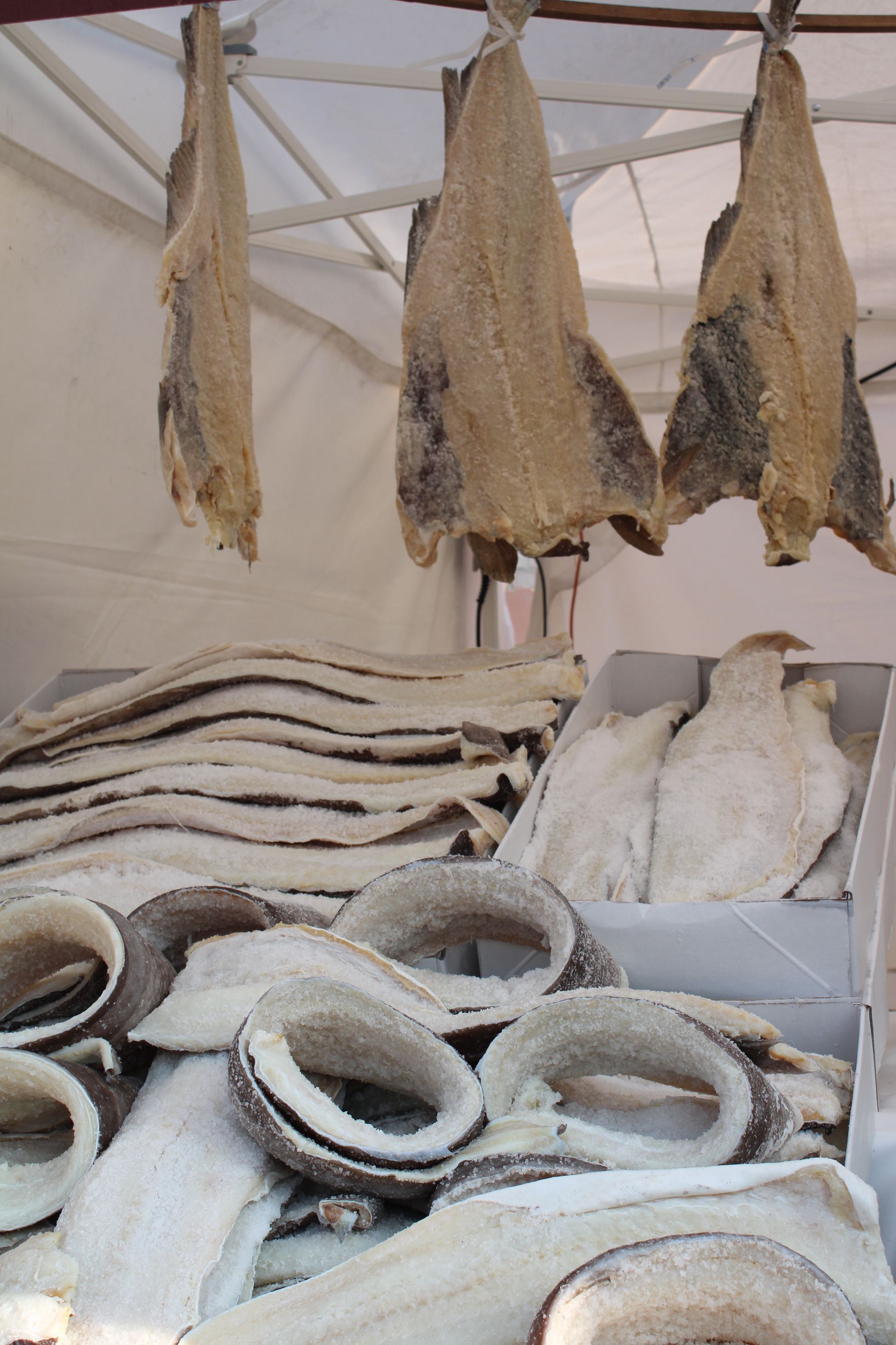 Pezzi di baccalà essiccato su una bancarella del mercato, alcuni appesi, altri impilati e altri ancora in un cesto.