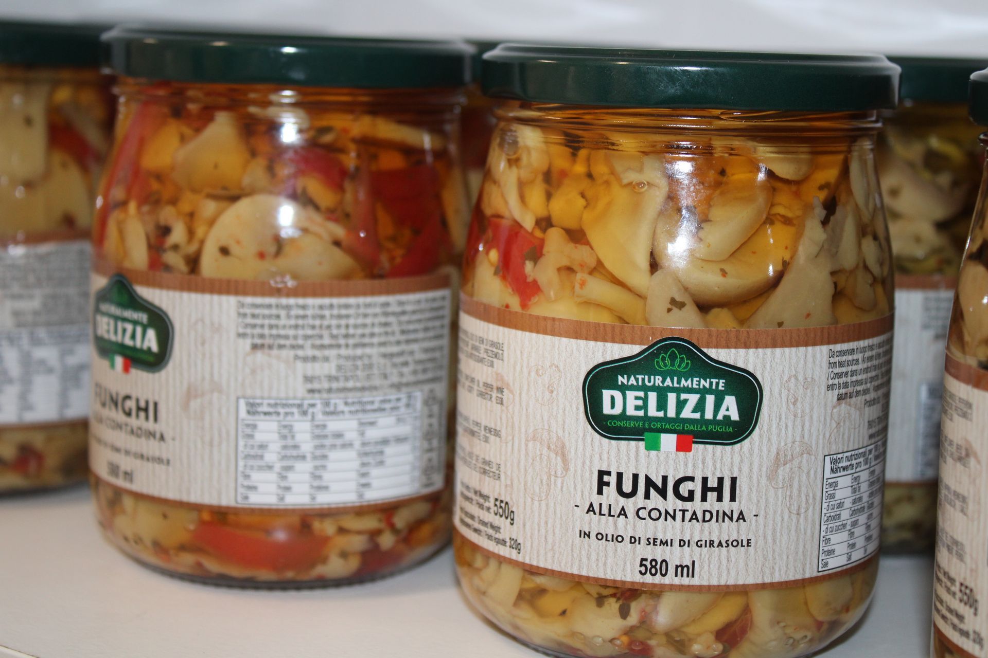 Vasetti di vetro di Delizia Funghi al la Contadina, pieni di funghi e verdure, su uno scaffale.