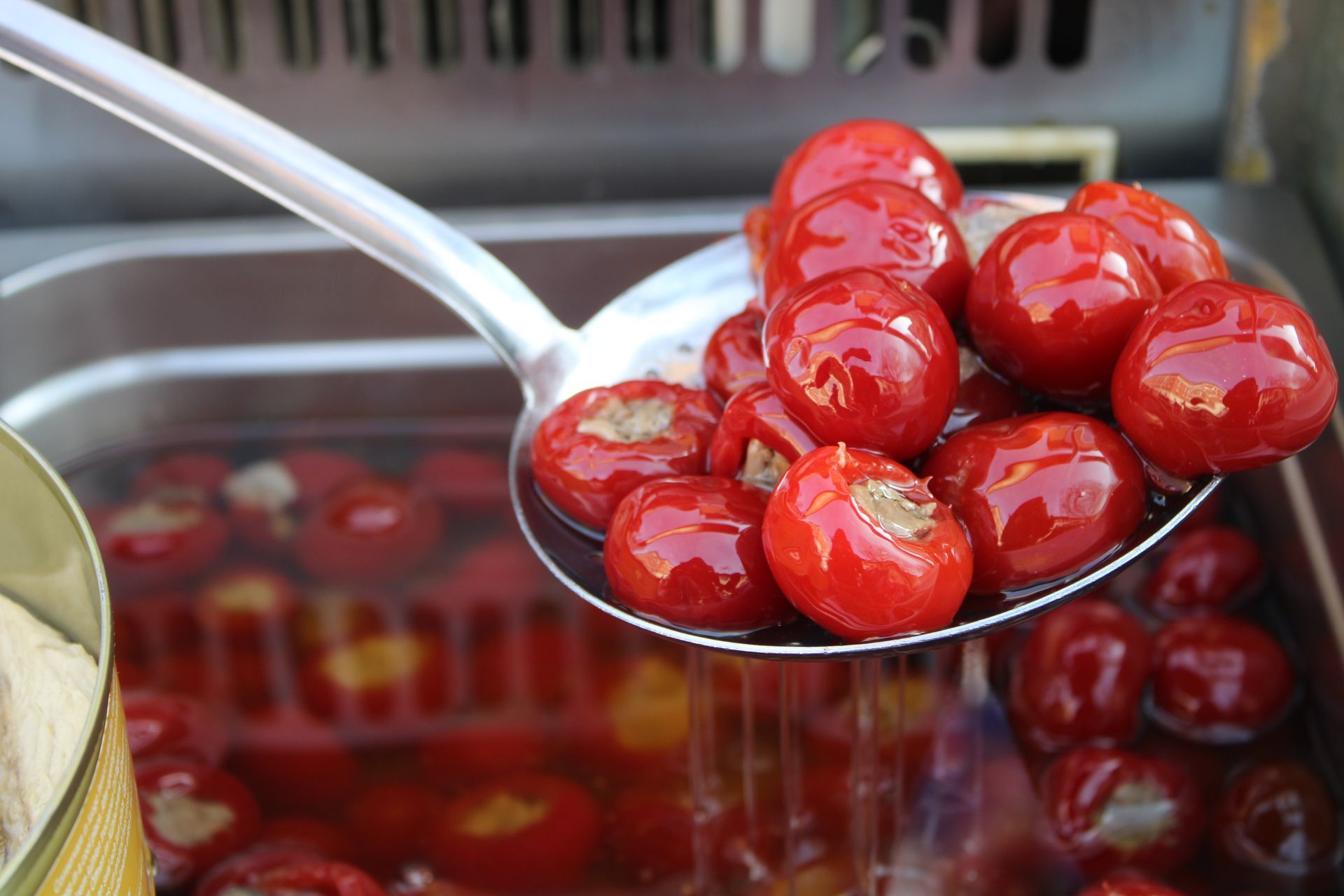 Un colino di metallo che raccoglie peperoncini rossi, rotondi e ripieni da un bagno liquido.
