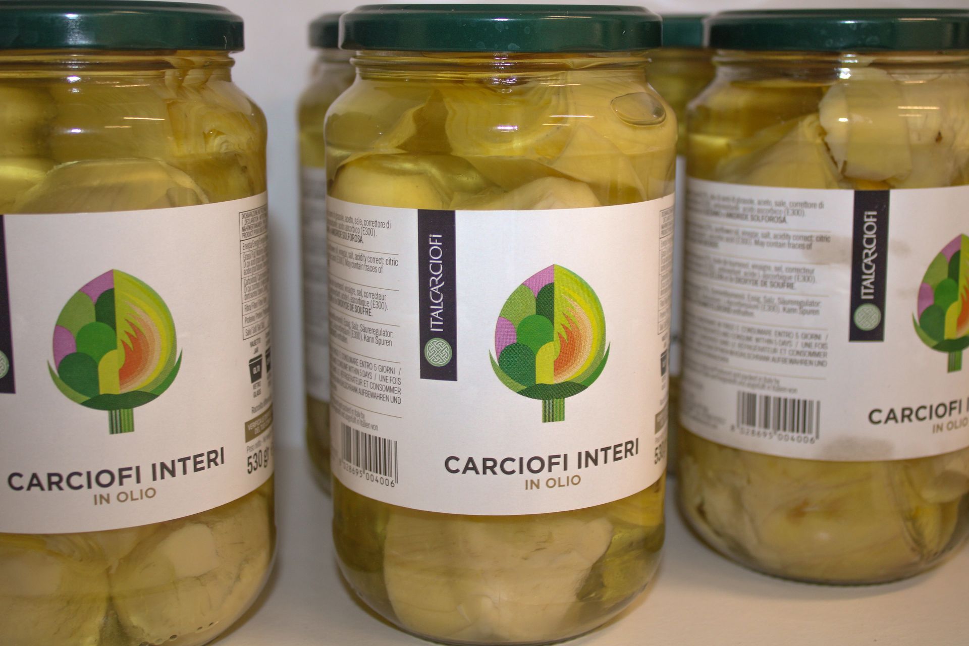 Vasetti di vetro con cuori di carciofo sott'olio. Ogni barattolo ha un'etichetta con il disegno di un carciofo.