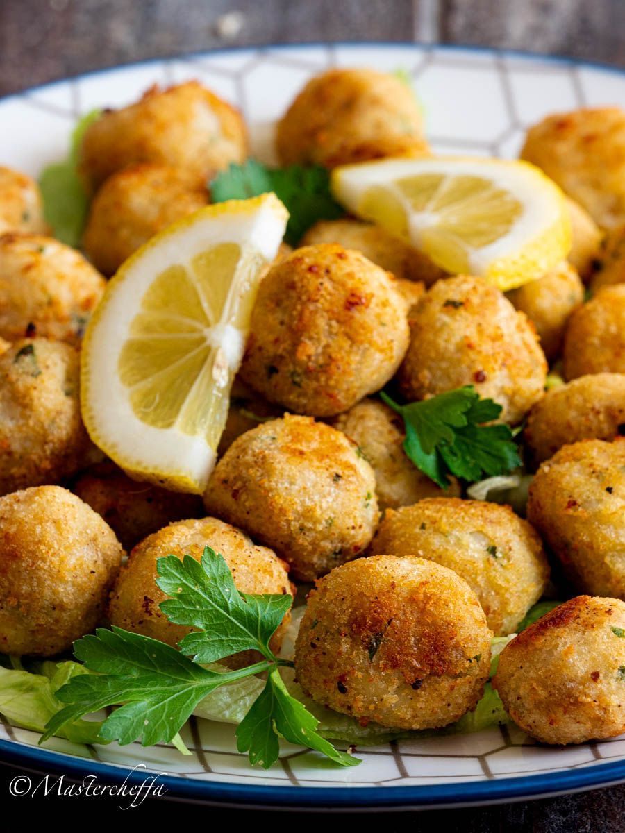 Polpette di pesce fritte dorate con spicchi di limone e prezzemolo su un piatto.