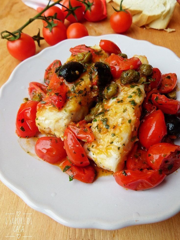 Piatto bianco di pesce al forno, con pomodori, olive, capperi ed erbe aromatiche.