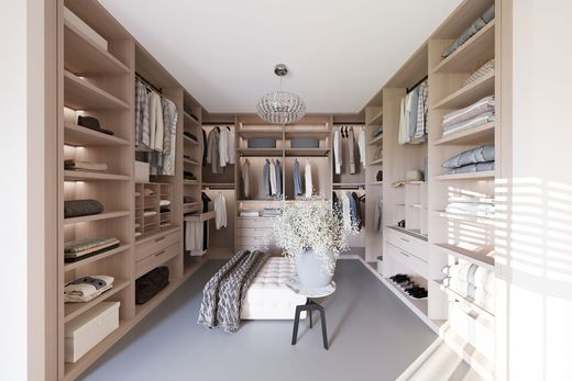 Walk-in closet with beige shelving, clothes, and a bench. A chandelier hangs from the ceiling.