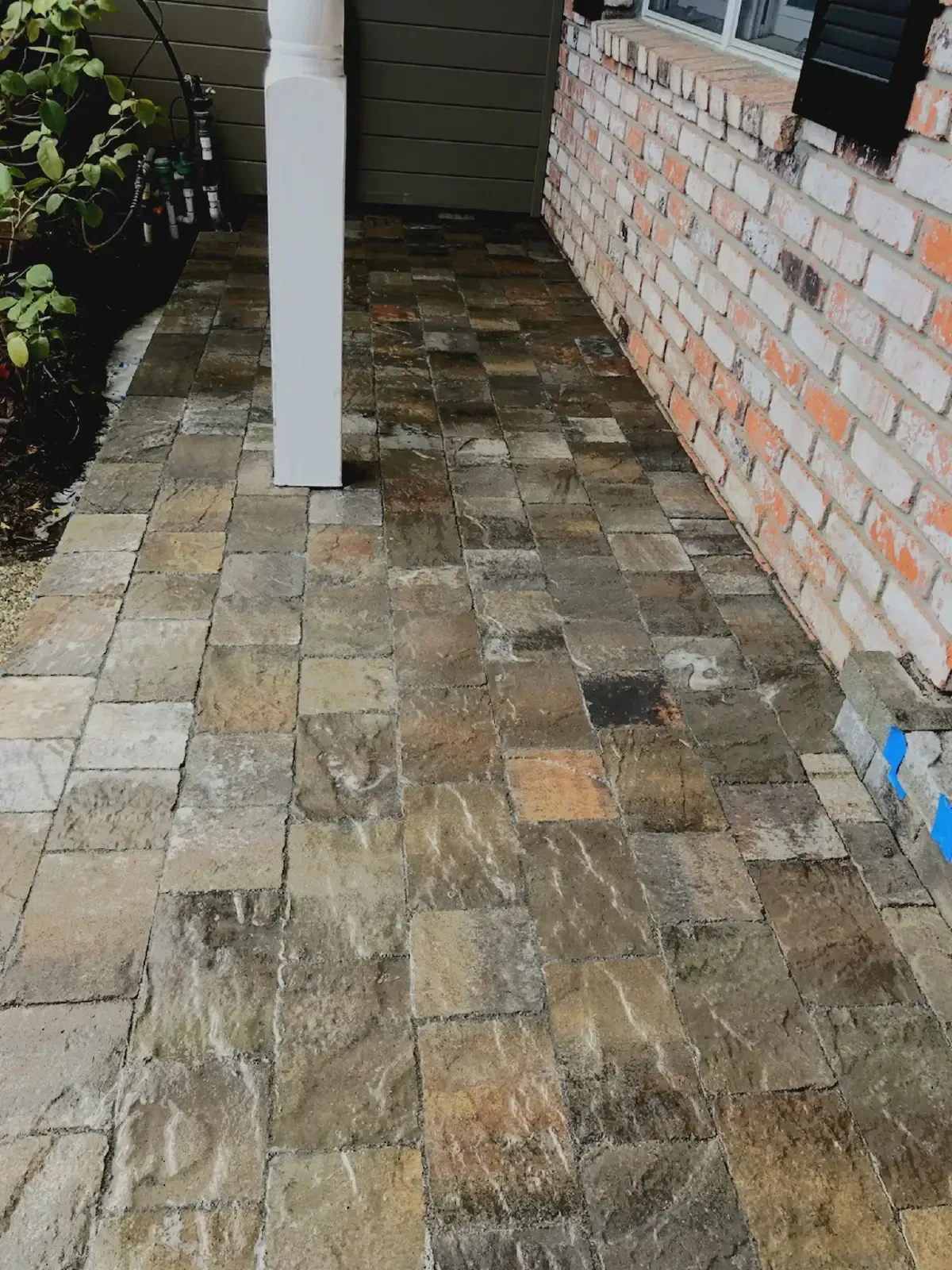 Stone paver walkway next to brick wall and white column.