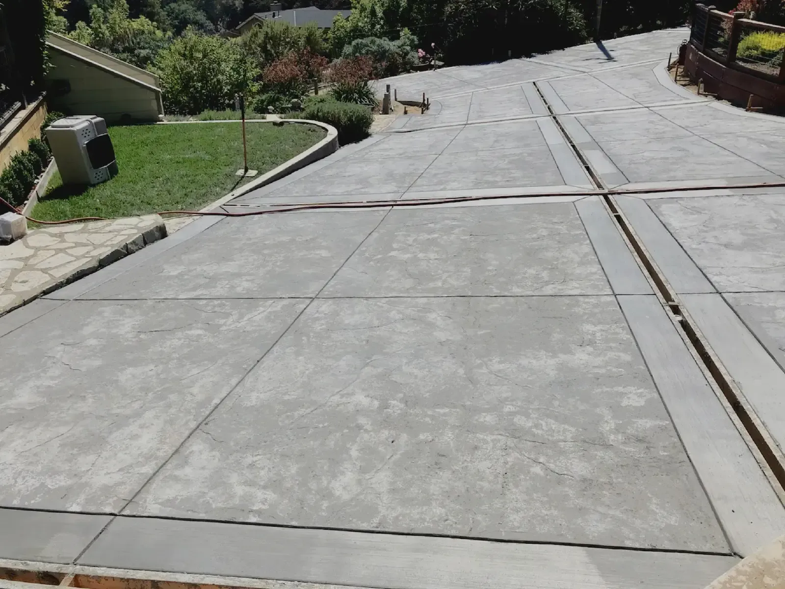 Concrete driveway with dividing lines, sloping uphill, with grass and greenery visible.