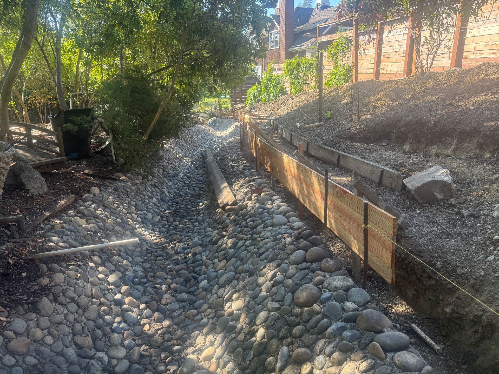 A rocky dry creek bed with wooden retaining wall and hillside garden.