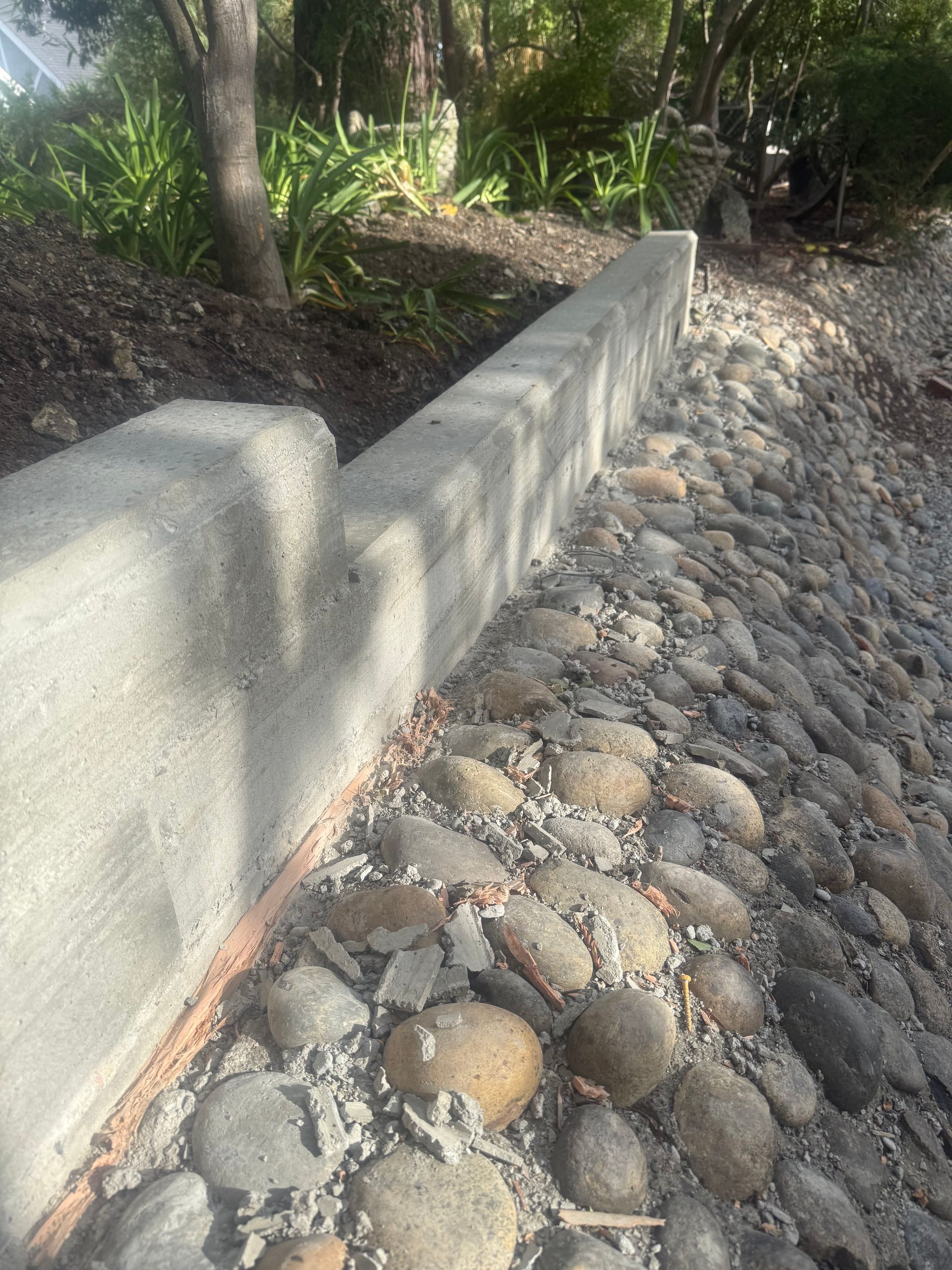 Concrete retaining wall bordering a slope covered in smooth, rounded rocks.