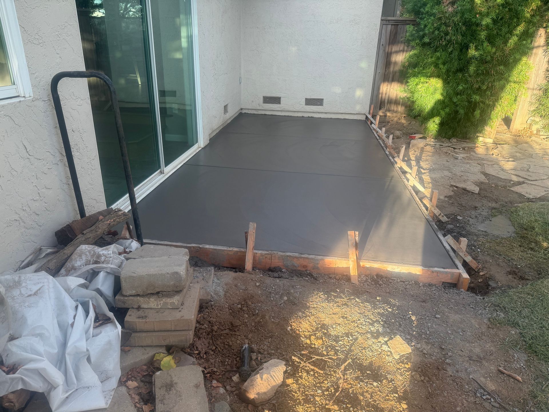 Newly poured concrete patio next to a sliding glass door. Wooden forms still in place.