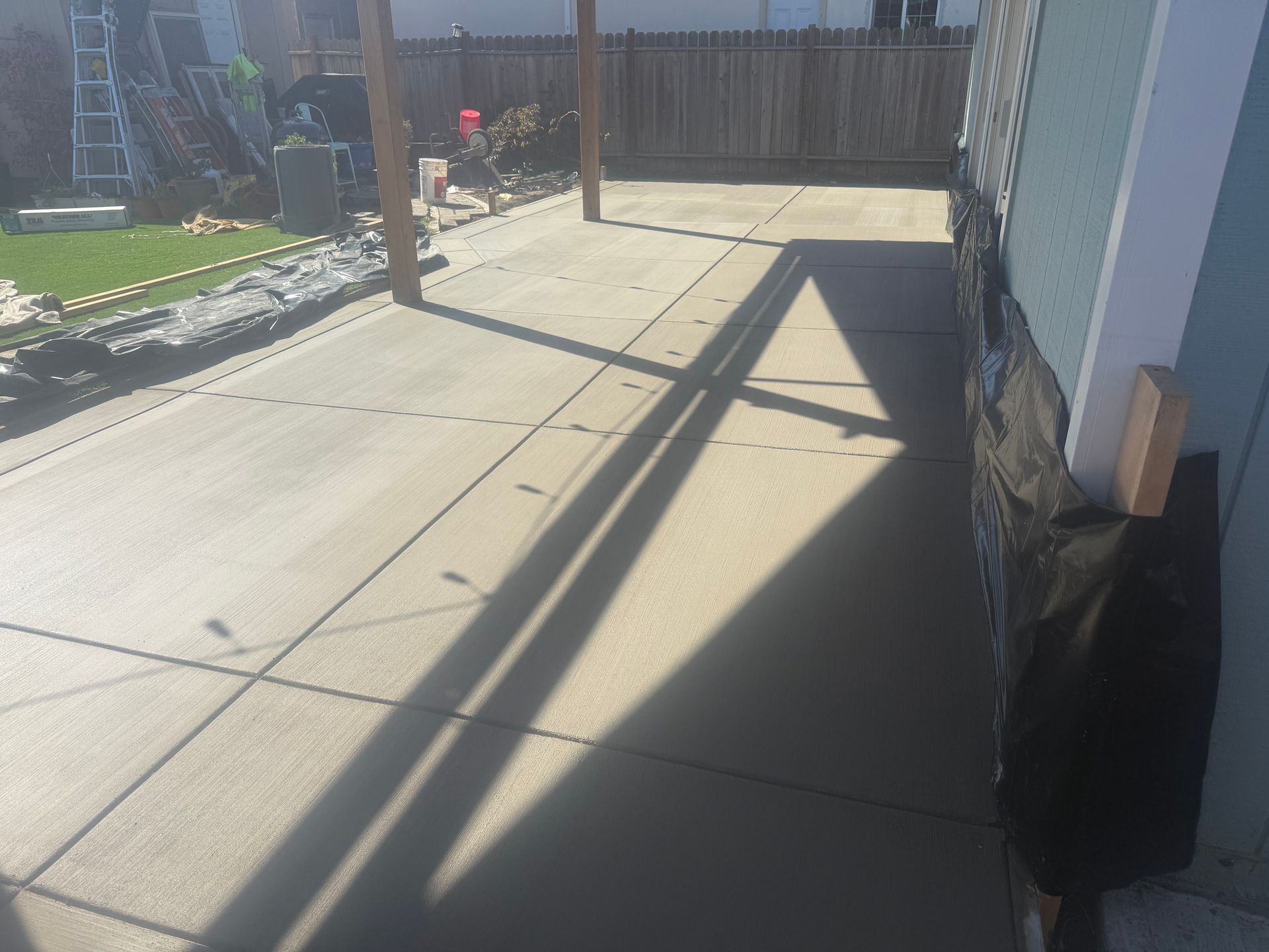 Concrete patio with pergola, next to a building wall.