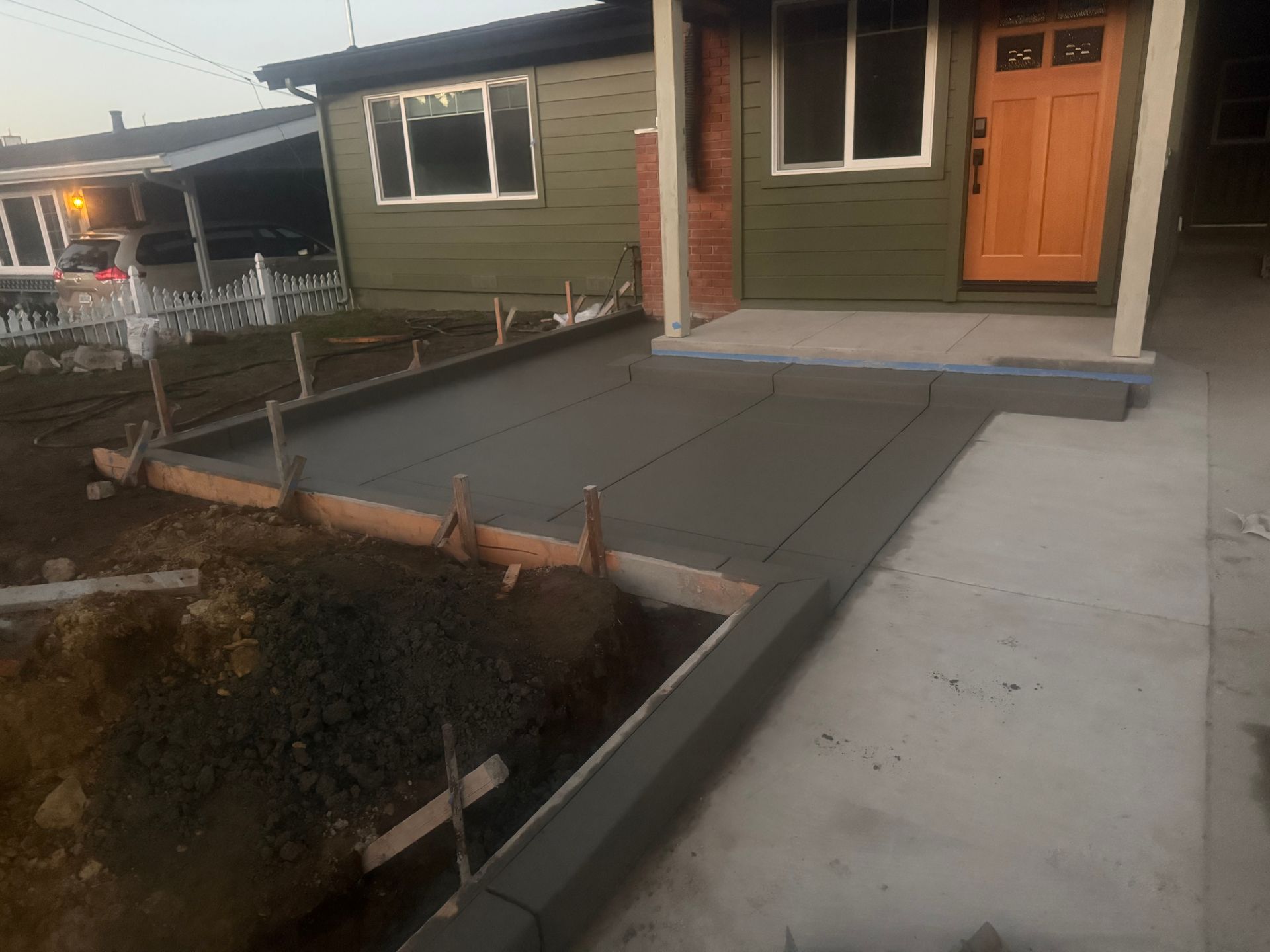 Newly poured concrete walkway and porch in front of a house, with wooden forms still in place.