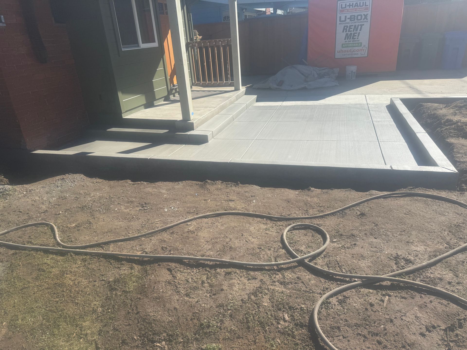 Concrete walkway leading to a building's entrance. A garden hose lies on the ground in front.