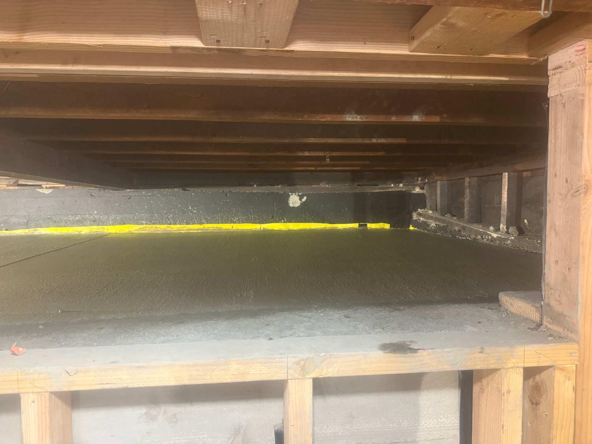 View from under a raised wooden floor showing gray gravel and yellow line.