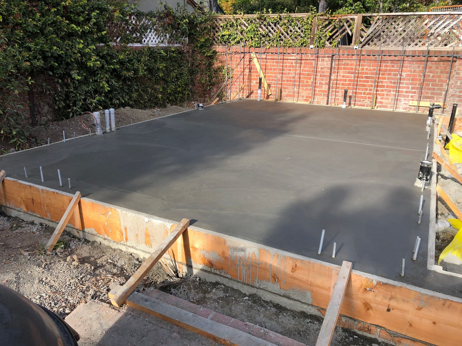 Freshly poured concrete slab within wooden forms, surrounded by gravel and brick wall.