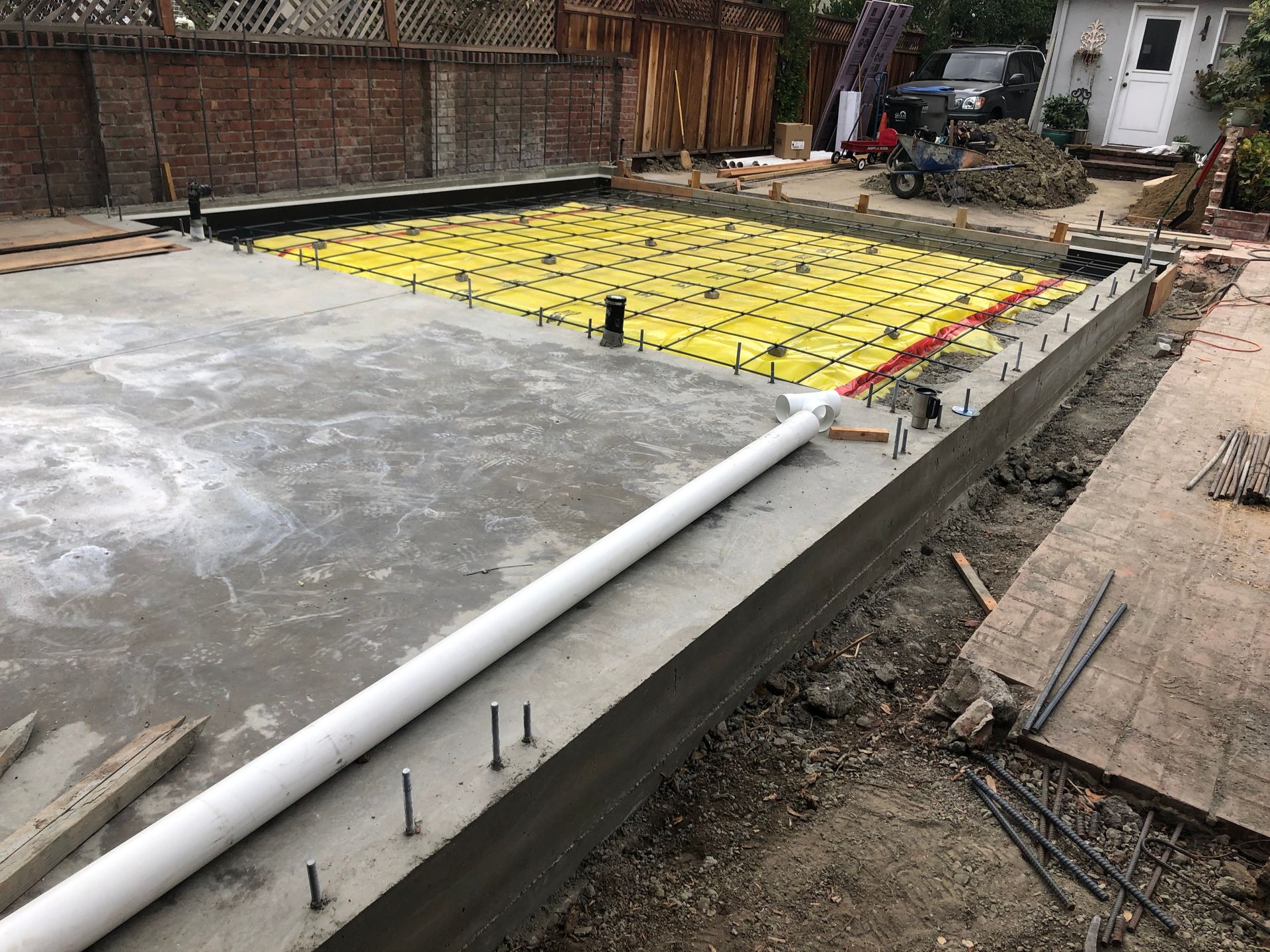 Concrete foundation with a yellow grid, plumbing, and a white pipe. Construction site outdoors.
