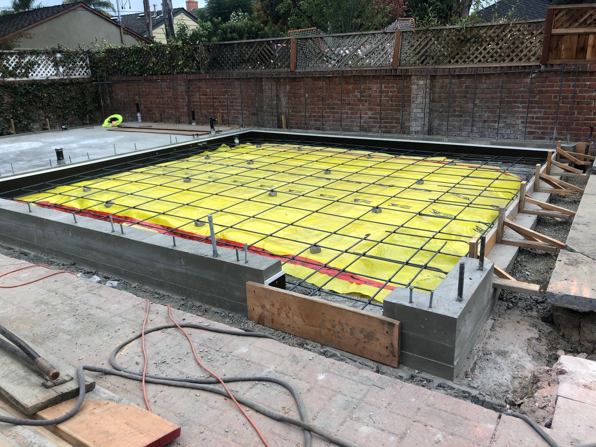 Construction site with a concrete foundation, yellow mesh, rebar, and wooden forms.