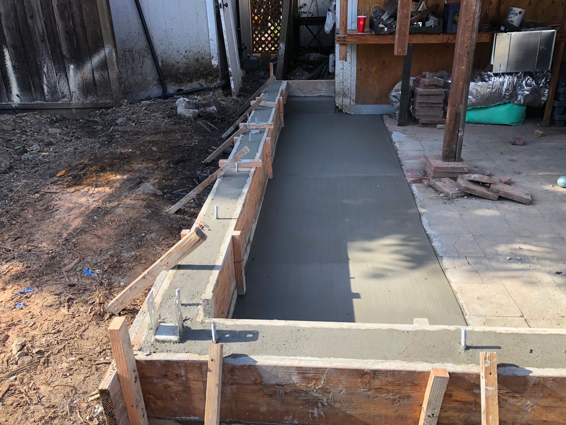 Concrete pathway construction in progress, with wooden forms in a backyard setting.