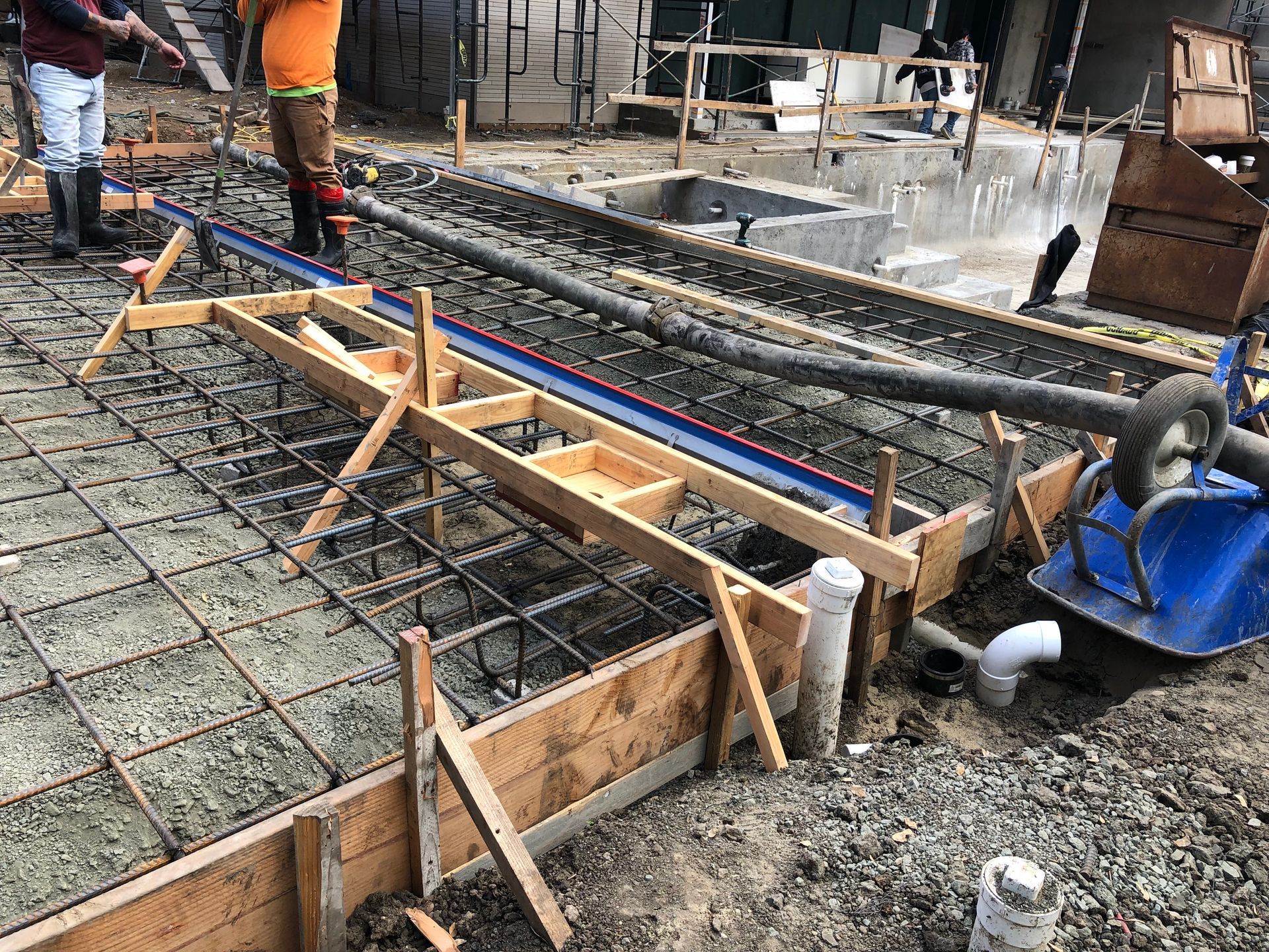 Construction workers pouring concrete, framing a foundation with rebar and forms.
