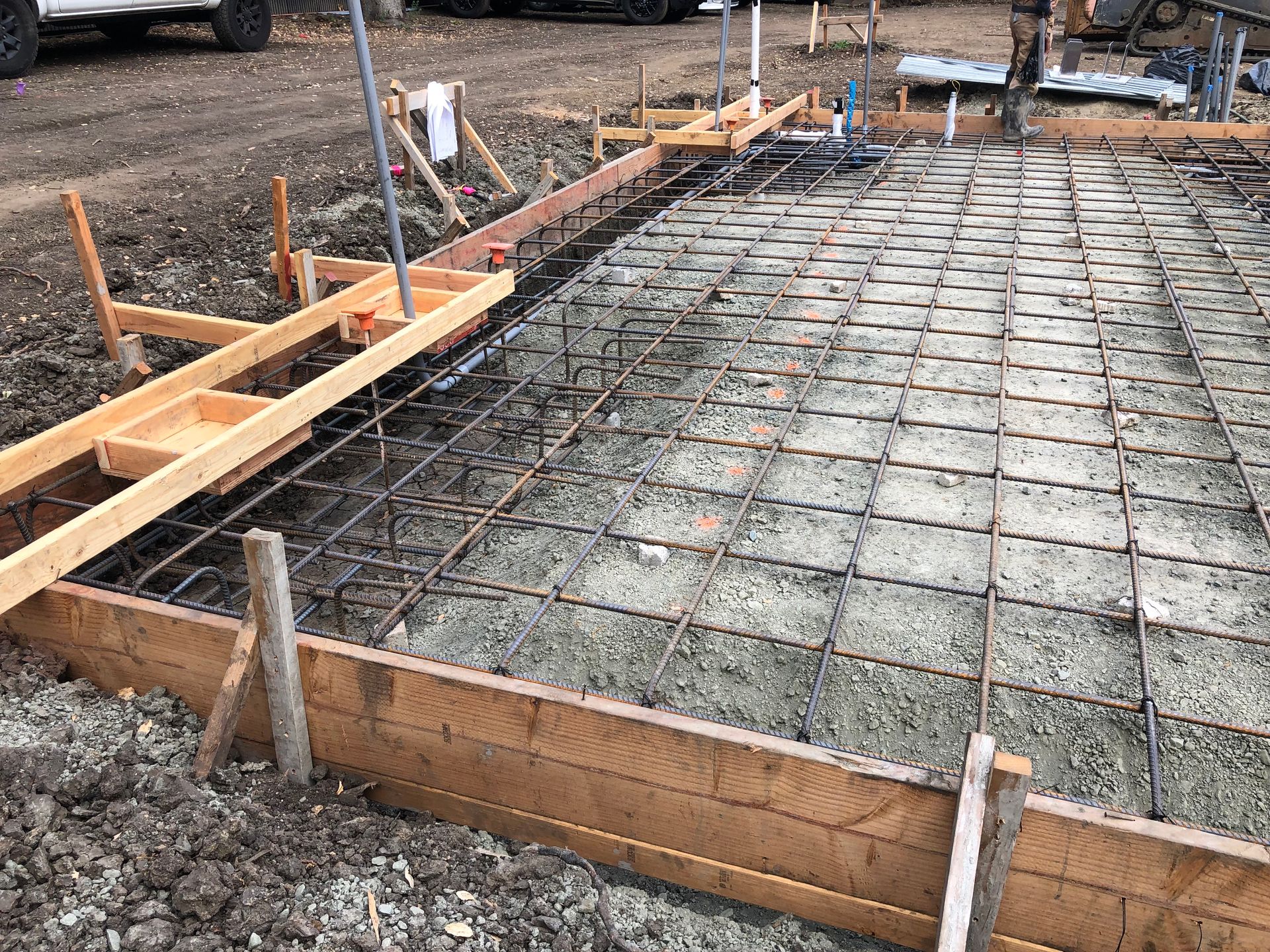 Construction site: wooden forms, rebar grid, and gravel base prepared for a concrete slab.