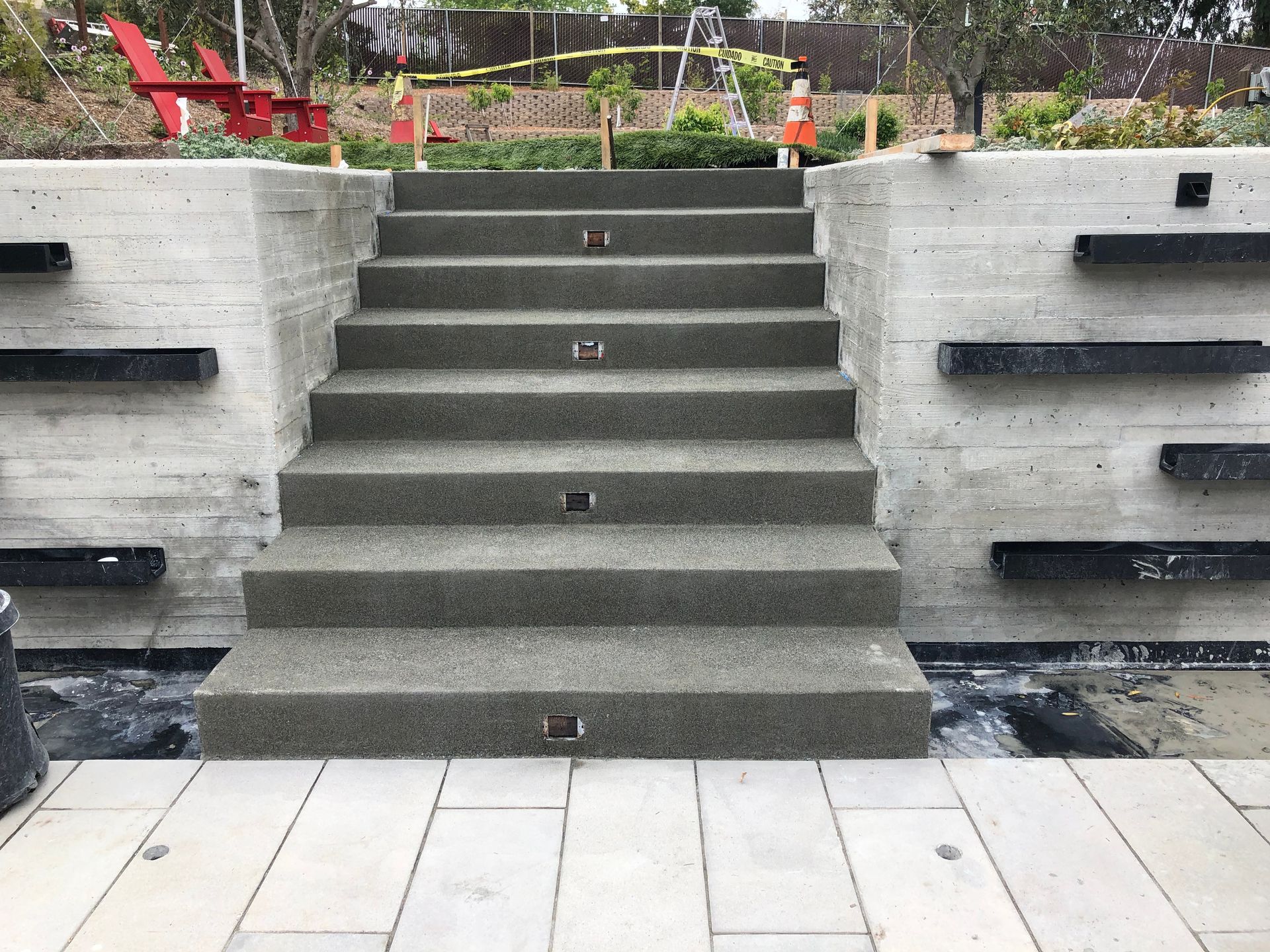 Concrete stairs leading up, flanked by concrete walls with black ledges. Outdoor setting.