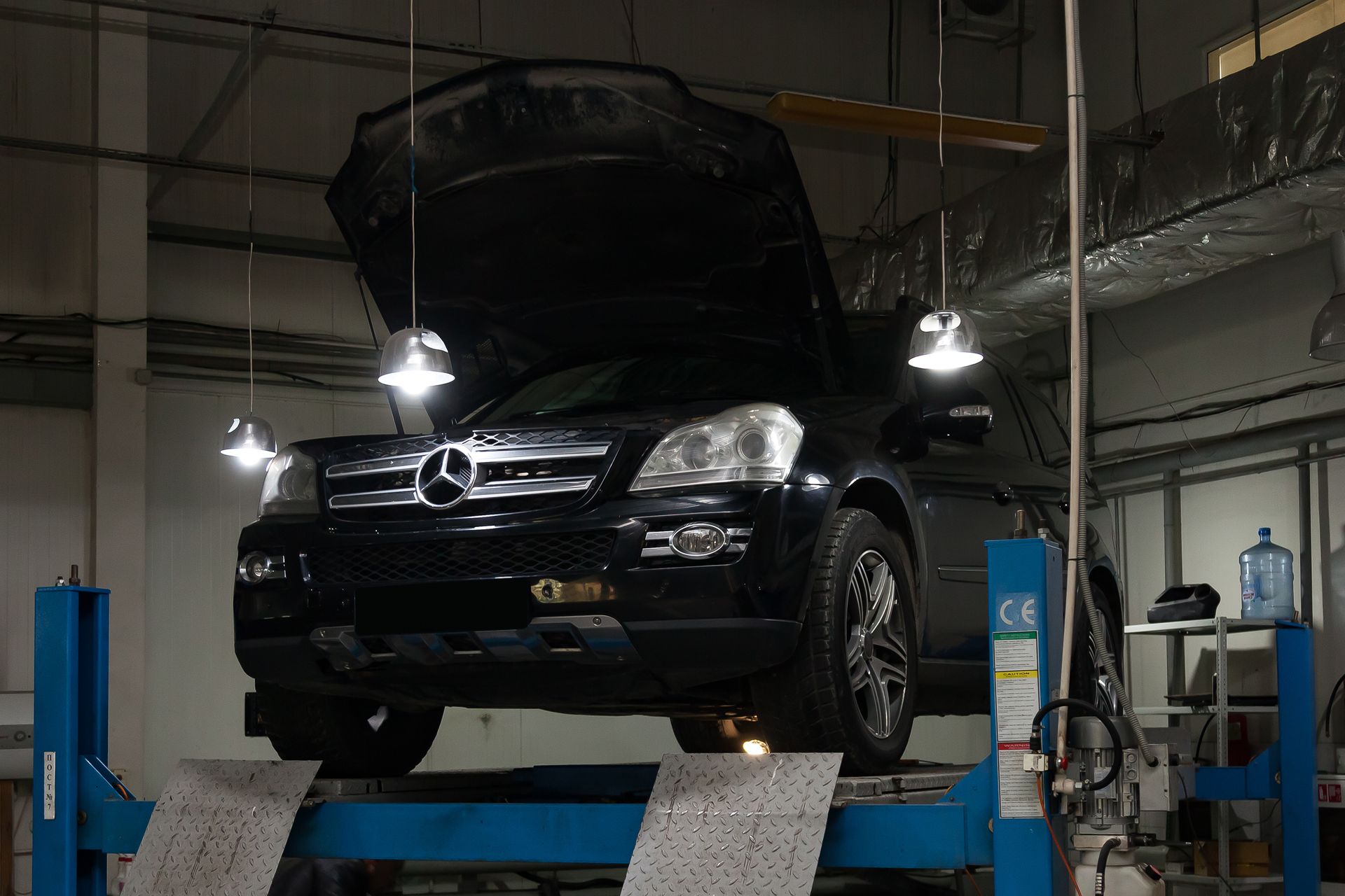 Black Mercedes SUV on a lift with hood open in a repair shop.