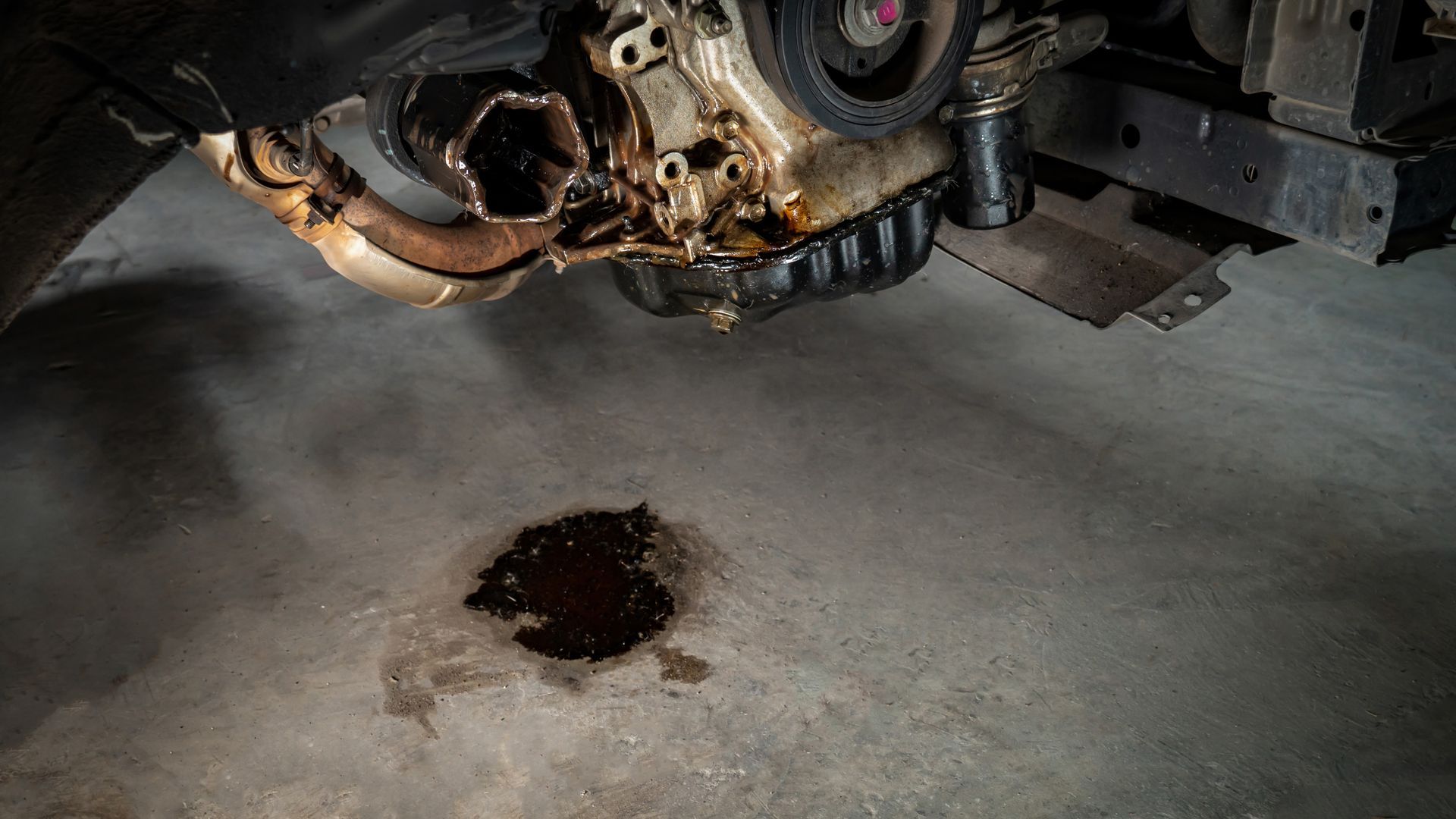 A close up of a car engine with a puddle of oil on the floor.