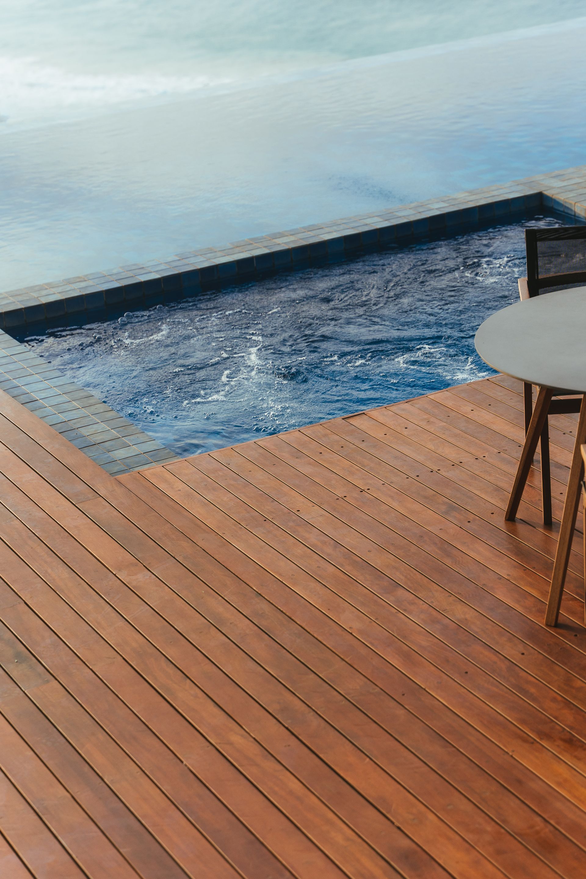 Um deck de madeira com mesa e cadeiras ao lado de uma piscina.