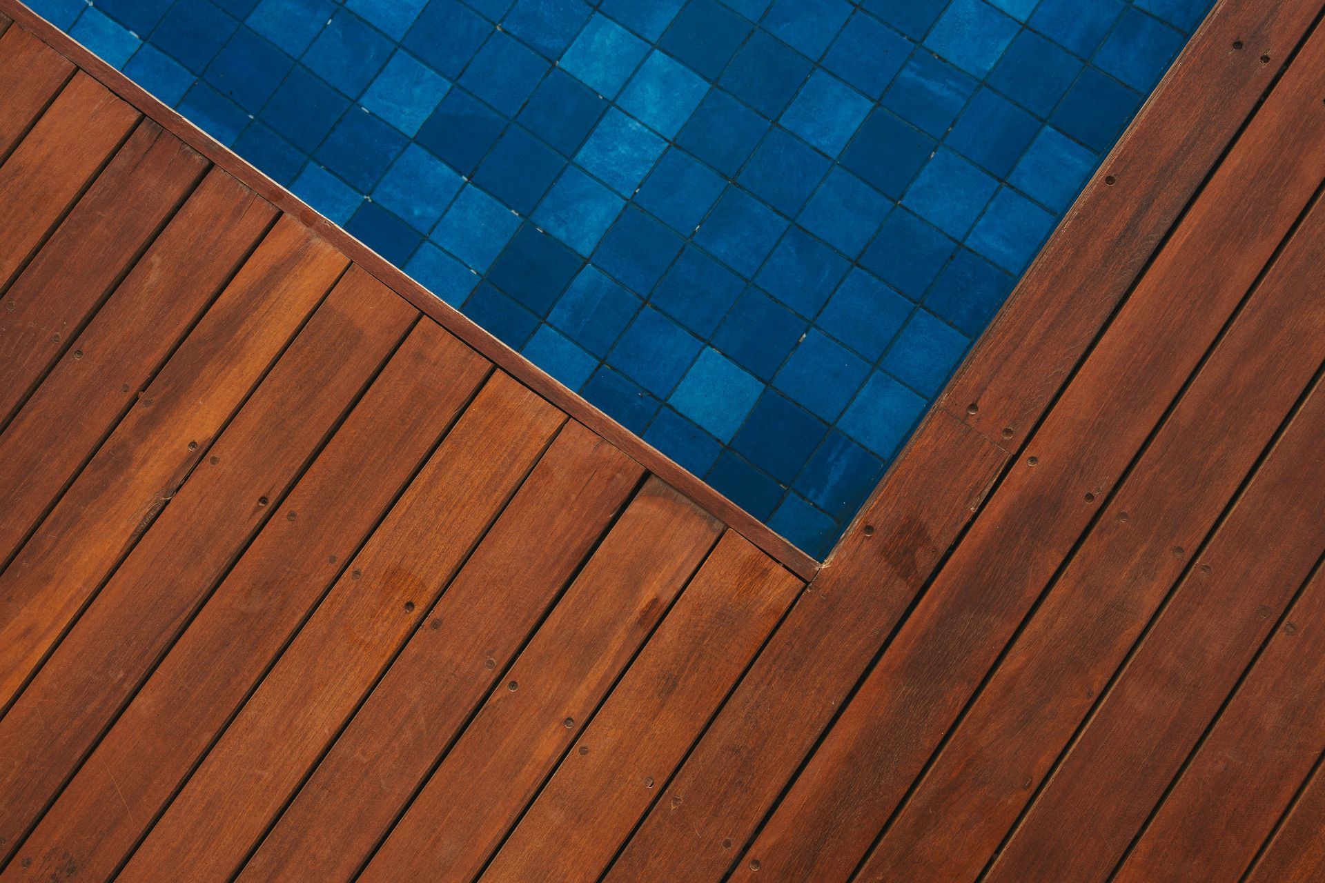 Um deck de madeira ao lado de uma piscina com azulejos azuis.