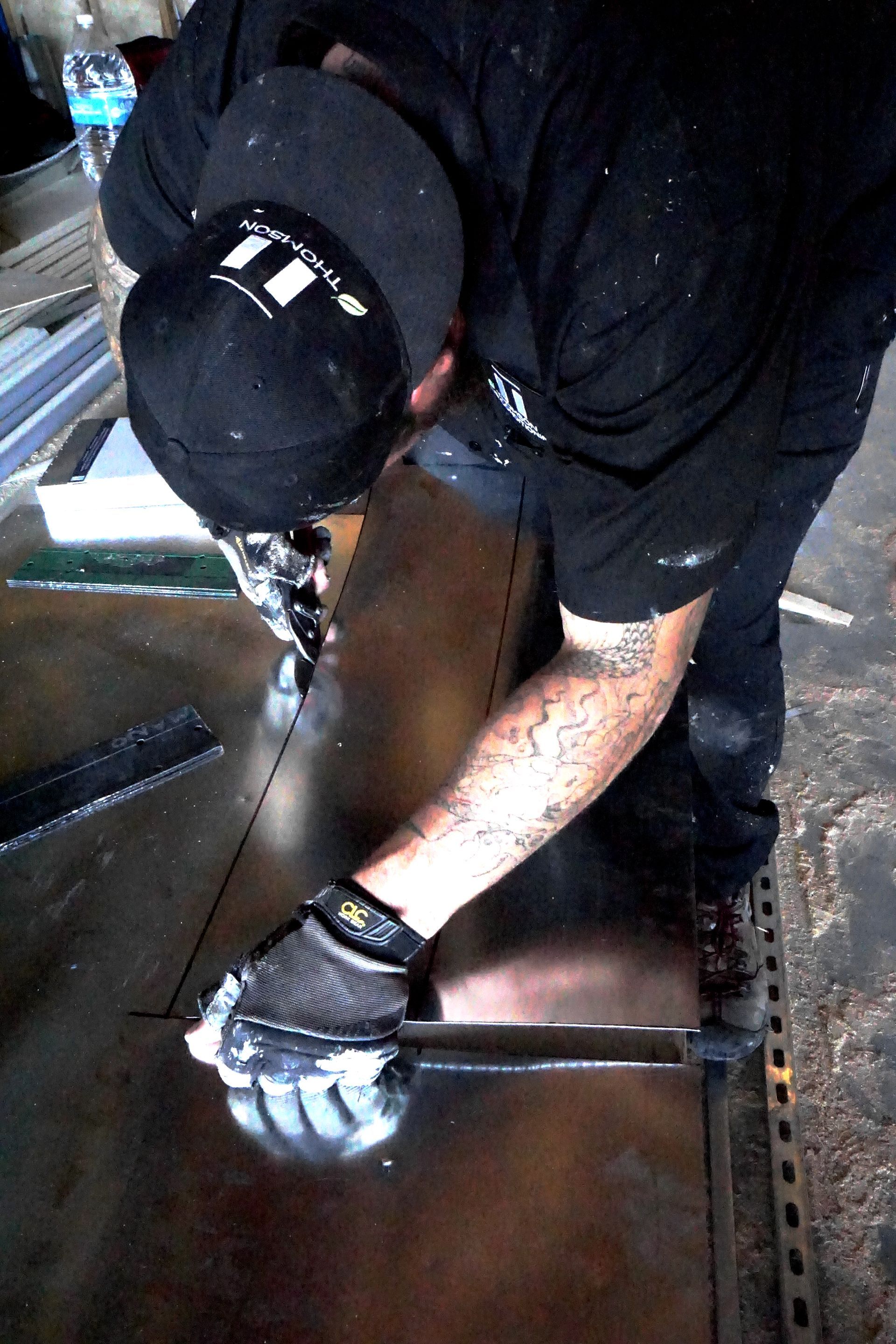 Two workers welding and grinding metal ductwork in a factory. Sparks and welding fumes are visible.