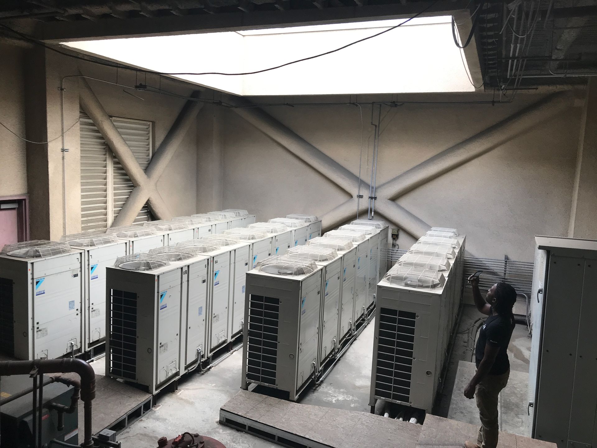 Two HVAC technicians in a mechanical room, one working on equipment, the other using a laptop.