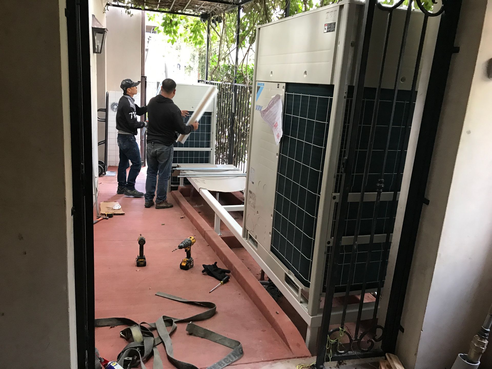 Two HVAC technicians working on equipment in a mechanical room, one using a laptop, the other inspecting wiring.
