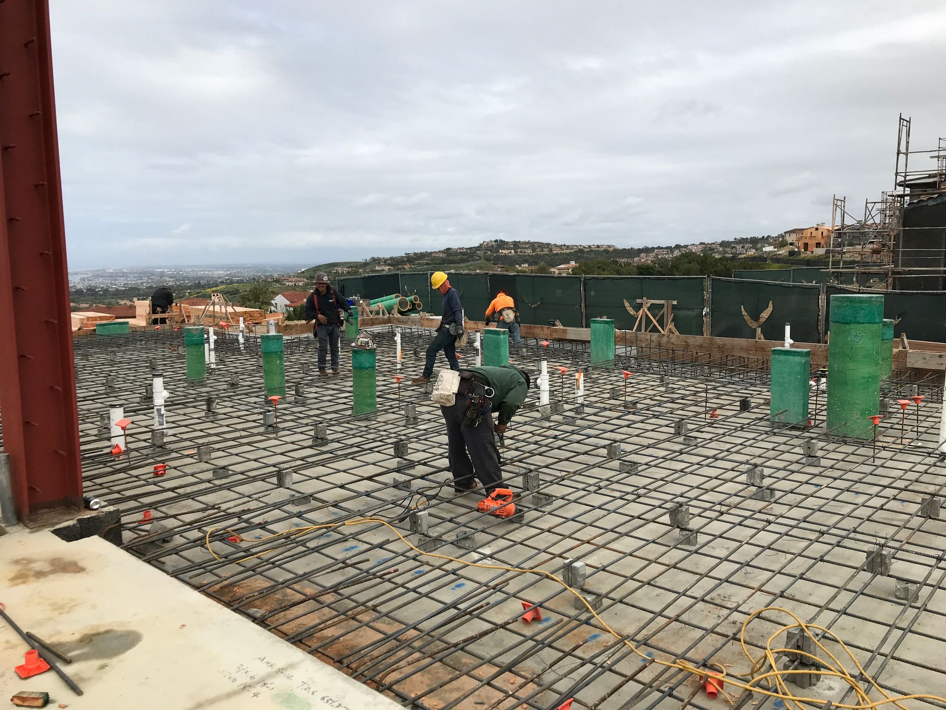 Four construction workers in hard hats examine blueprints at a worksite.