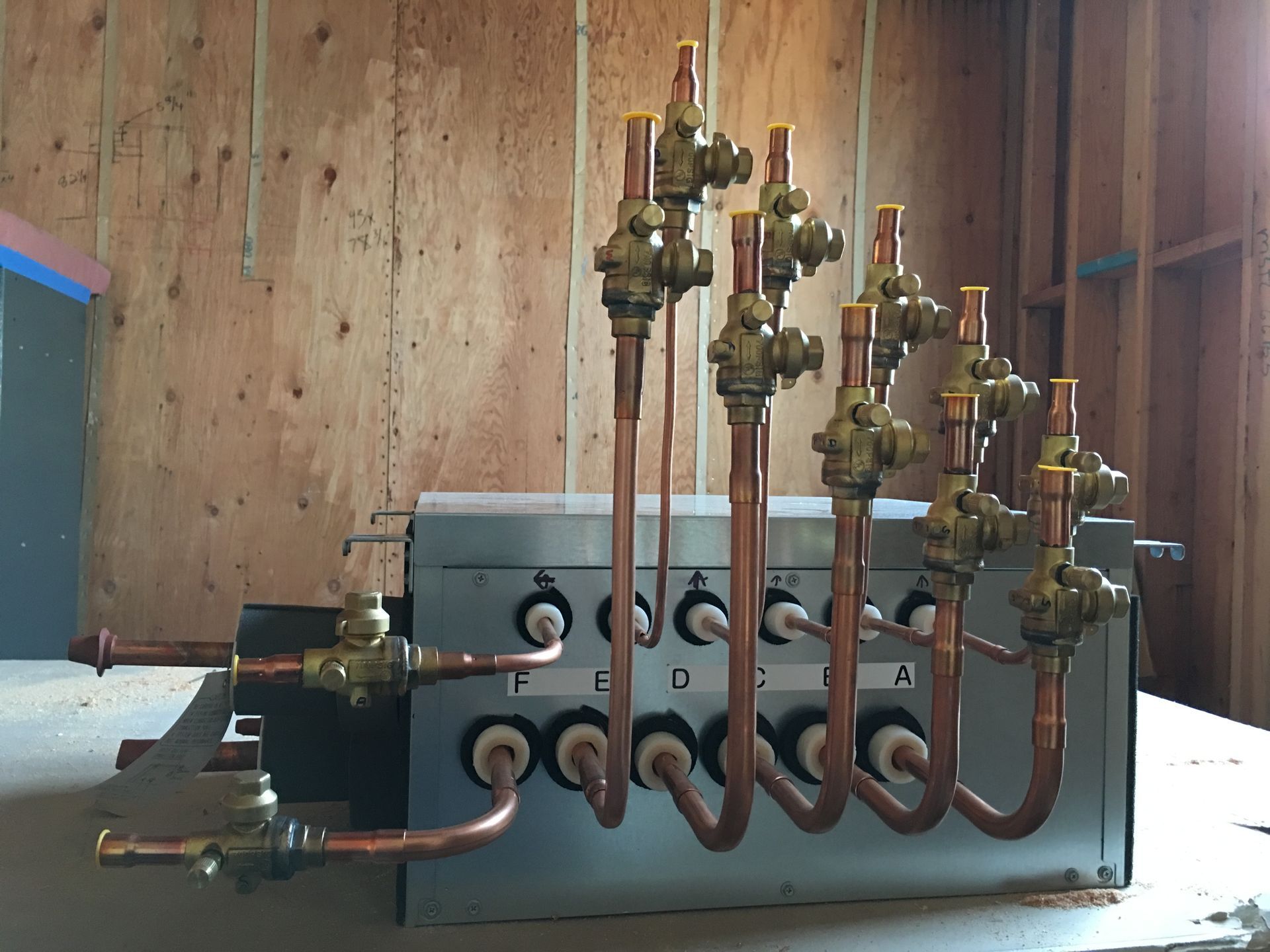 Two workers in a utility room, one at a control panel, the other using a tablet near red pipes.